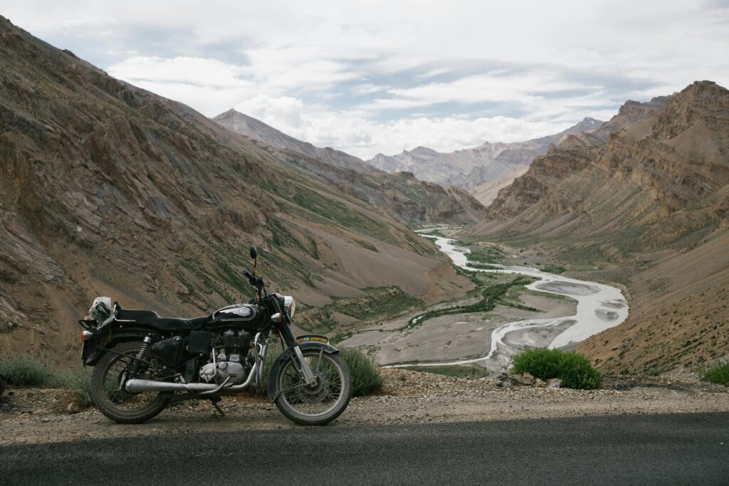 A motorcycle parked along a scenic road with a river winding through mountainous terrain, perfect for adventure trips.